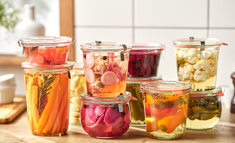 A photo of several stacked glass mason jars with pickled food inside, on a counter.