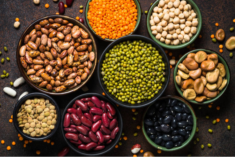 Legumes, lentils, chikpea and beans assortment in different bowls on stone table. Top view.